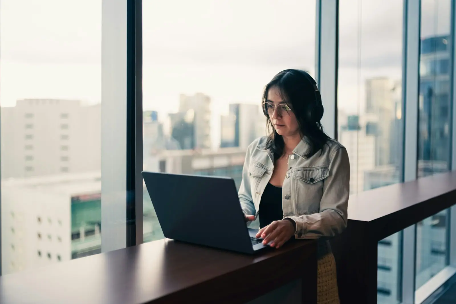 A woman working on a laptop at a window overlooking the city